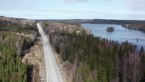 drone shot of swedish highway running through forest, cars driving by with lake in background