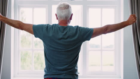 senior man opens curtains and stretches in front of window