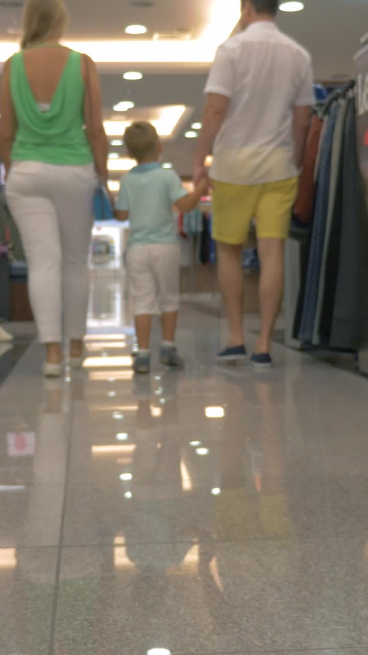 Keluarga dengan Anak Berjalan Melintasi Lorong Pusat Perbelanjaan yang Terang