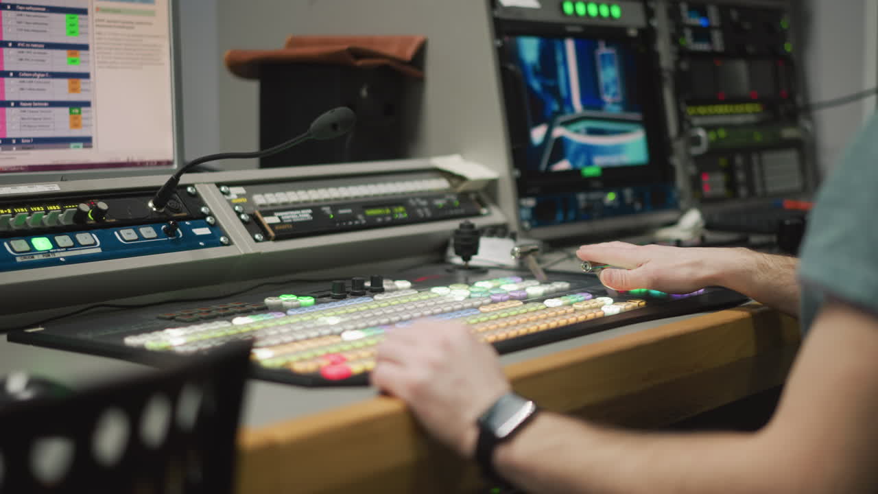 Close-up of hand operating video production switcher in broadcast studio. Professional television equipment with illuminated buttons and monitor in control room environment