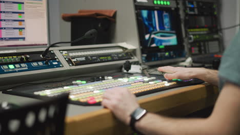 close-up of hand operating video production switcher in broadcast studio. professional television equipment with illuminated buttons and monitor in control room environment