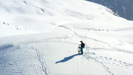 Aerial-view,-panning-around-a-snowboarder-standing-on-top-of-a-snow-covered-mountain