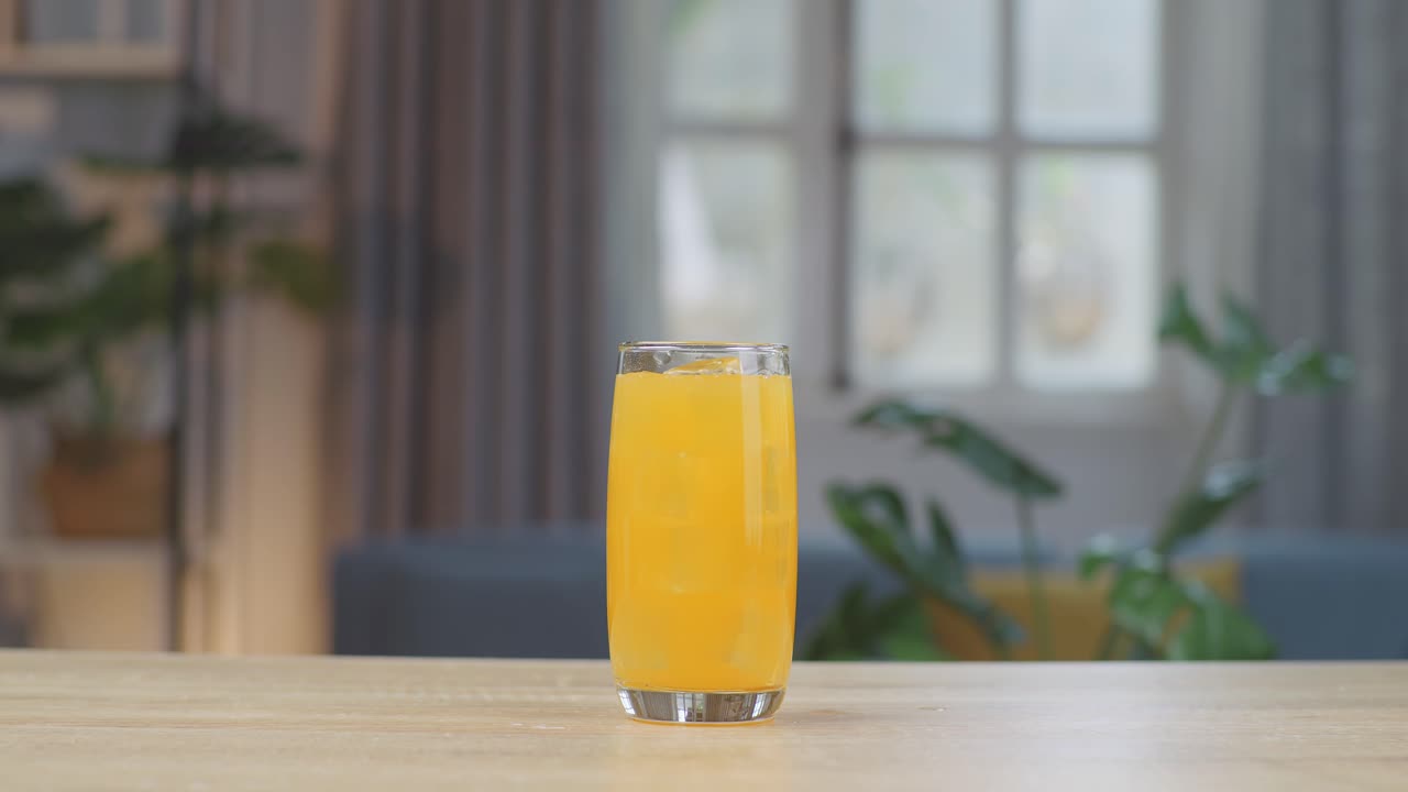cubos de hielo cayendo en un vaso de jugo de naranja en la mesa en casa