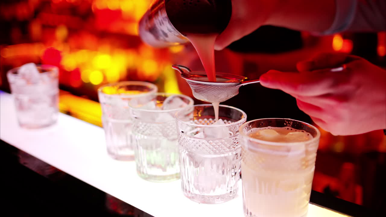 Barman making cocktails with whiskey liquor alcohol at the bar at night with red neon lights, slow motion