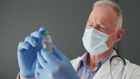 caucasian senior male doctor wearing face mask holding covid-19 vaccine