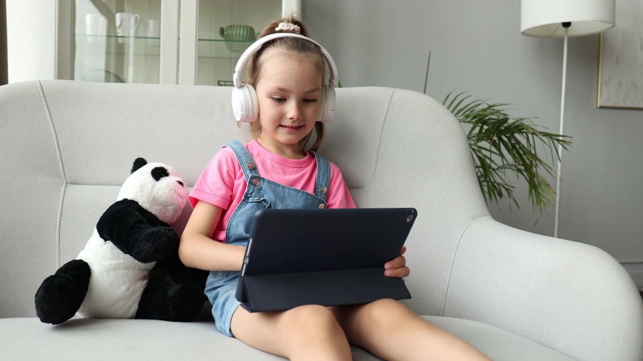 Jovem menina feliz com fones de ouvido usando tablet no sofá