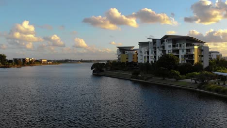 a drone flies through trees towards a beautiful resort over a bed of water at sunset