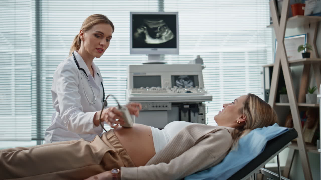 Doctor performing ultrasound pregnant patient. Medical professional reviewing