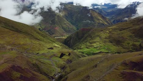 aerial, reverse, drone shot, rising over green hills, roads, fog and geographical formations, in the andes mountains, on a overcast day, near cuzco, in peru