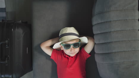 Cute-toddler-in-hat-with-hands-behind-head-rests-on-couch