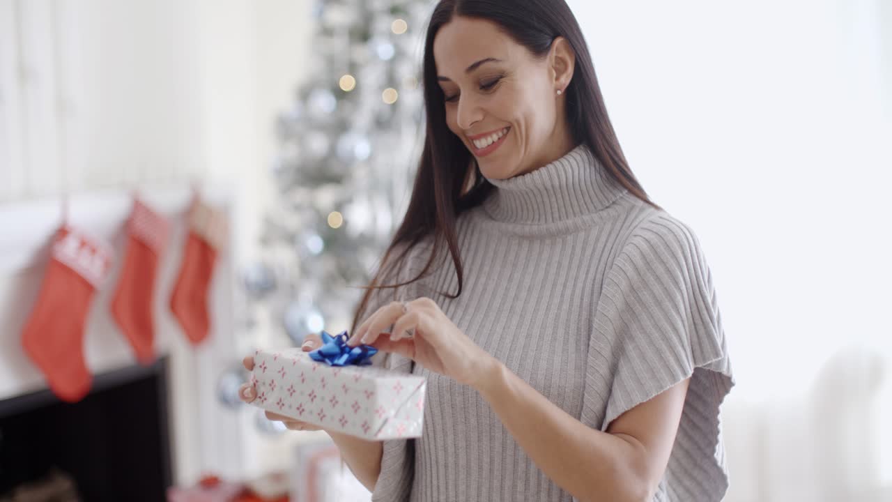 una joven sonriente abriendo un regalo de navidad