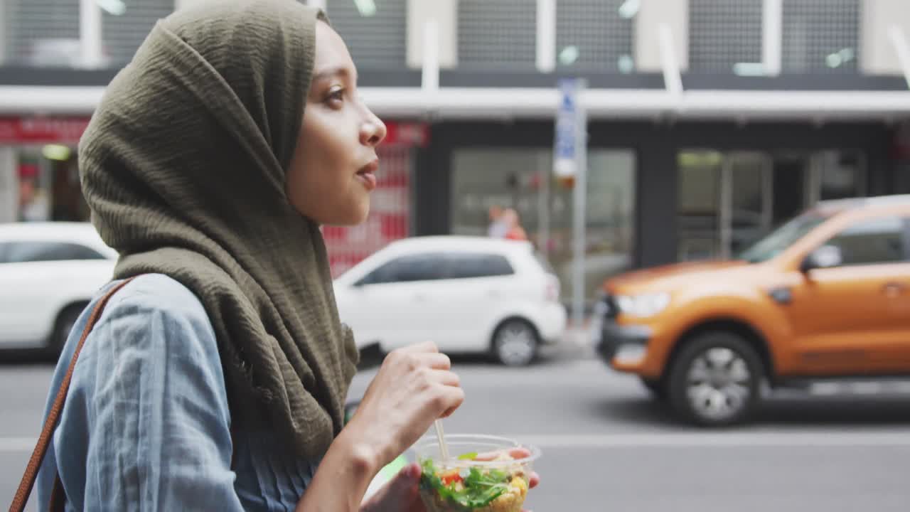 mujer con hijab comiendo una ensalada para llevar caminando por la calle