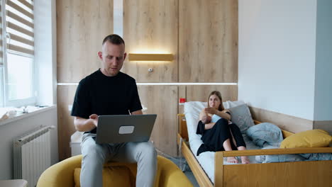 married couple arguing about laptop usage. man is focused on work while woman has to take care of baby.