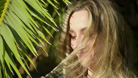 Close-up-of-the-lovely-smiling-young-blonde-woman-posing-to-the-camera-with-palm-branch