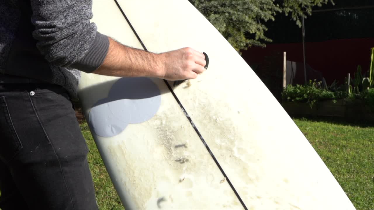 Surfer removing wax from board in home garden