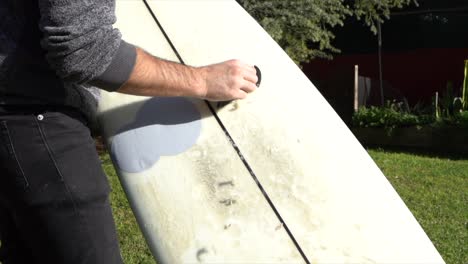 surfer removing wax from board in home garden