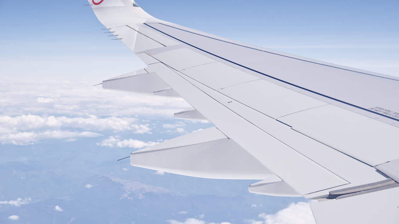 Bright window seat view of an airliner wing cruising above a sea of clouds under a clear blue sky