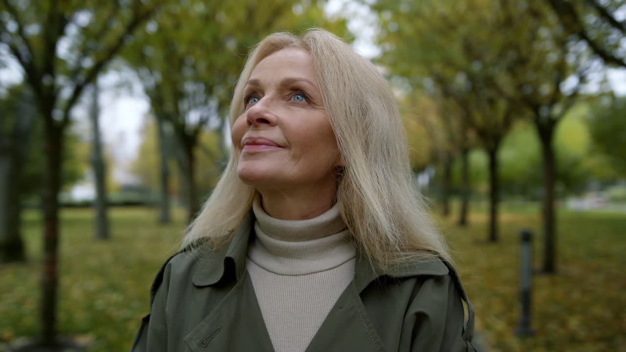 Portrait of romantic woman looking into sky through trees branches in park .