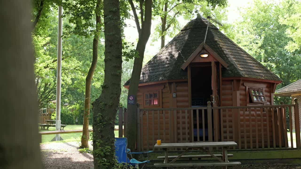 Smooth vertical camera slide of cozy log cabin surrounded by lush green trees.