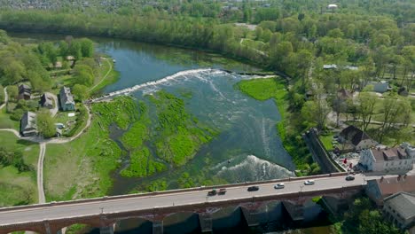 Aerial-establishing-view-of-old-red-brick-bridge-over-the-Venta-river-,sunny-summer-day,-drone-shot-moving-forward,-tilt-down