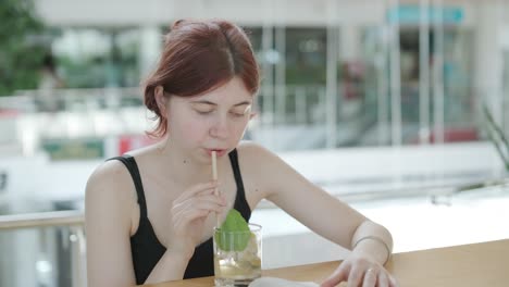 young woman reading a book and sipping a cocktail with a straw at a wooden counter in a bright, modern cafe with natural light. relaxed and focused ambiance