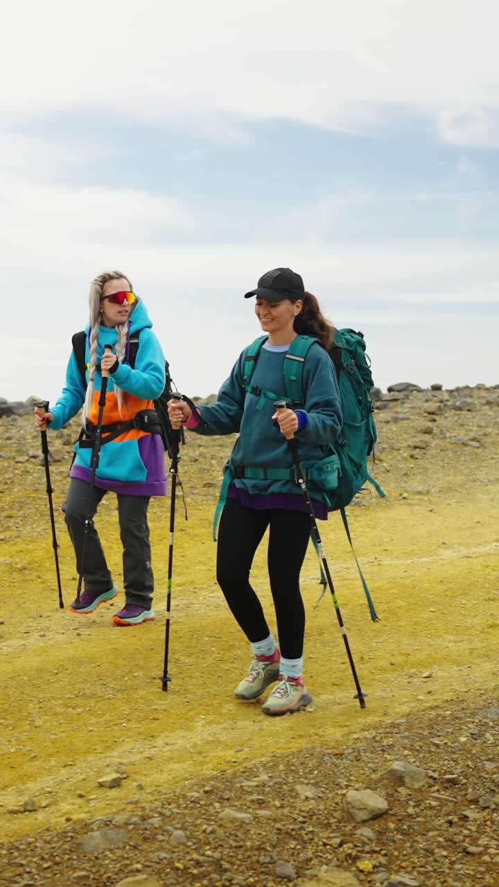 Due donne che fanno escursioni con zaini e bastoncini da trekking su terreno roccioso giallo