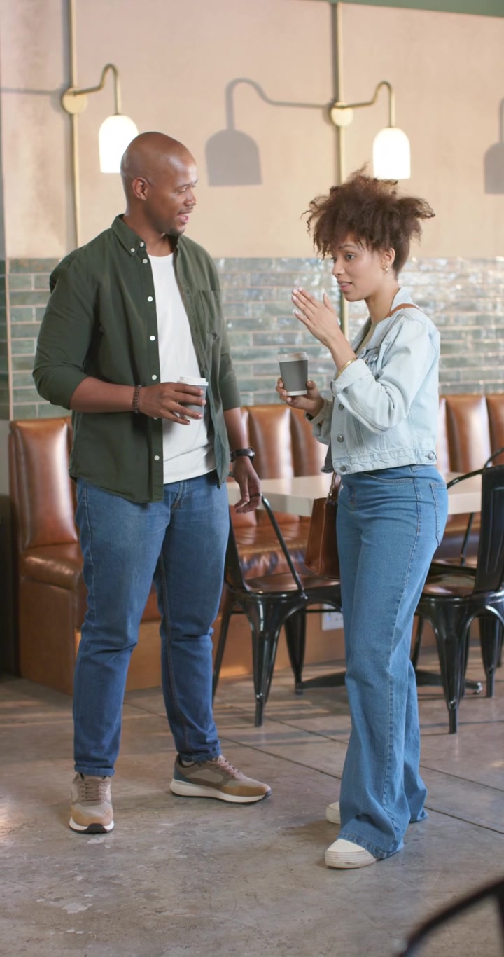 Vertical video: African American friends in cafe holding to-go cups woman raising cup starting chat