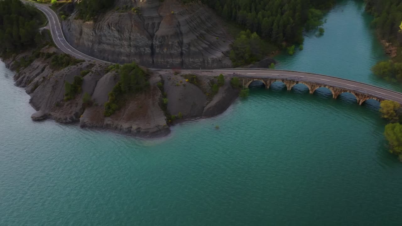 Drone che segue i ciclisti su un ponte ad arco sopra le acque turchesi vicino all'Antiguo Balneario de Tiermas, Embalse de Yesa Reservoir, Aragona, nella zona del corridoio del Camino de Santiago, Spagna