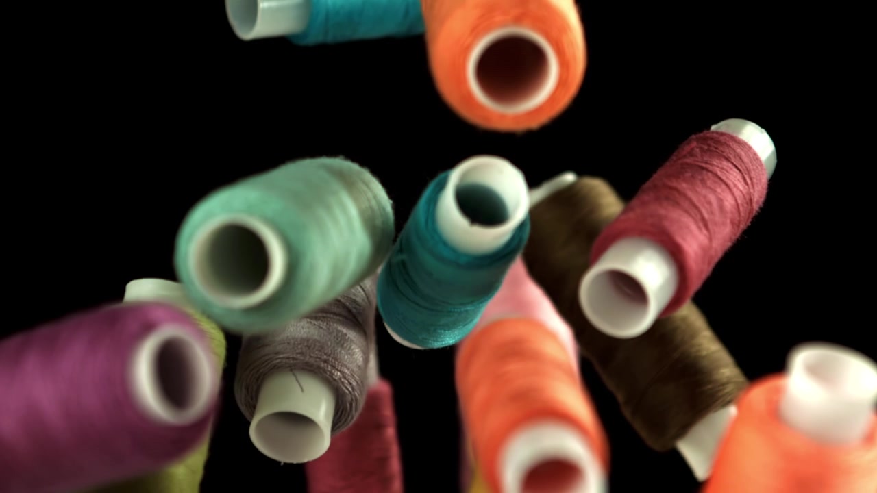 Colorful Spools of Thread Falling in Slow Motion Against a Black Background