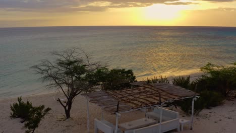 White-gazebo-with-thatched-roof-on-sandy-beach-at-sunset,-Dominican-Republic