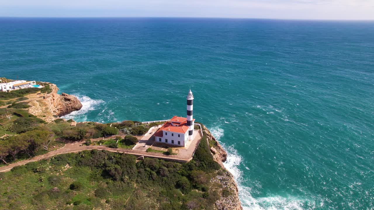 Drone footage of a black and white striped lighthouse on a cliff near Portocolom