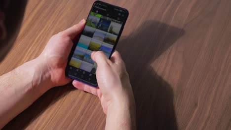 Man-Holding-a-Smartphone-at-a-Brown-Table-Scrolling-on-Social-Media