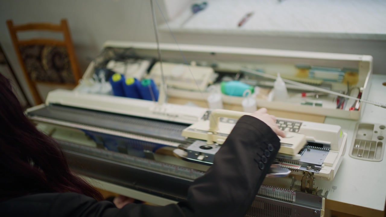 Close up of hands working with blue knitted fabric attached to a flatbed knitting machine