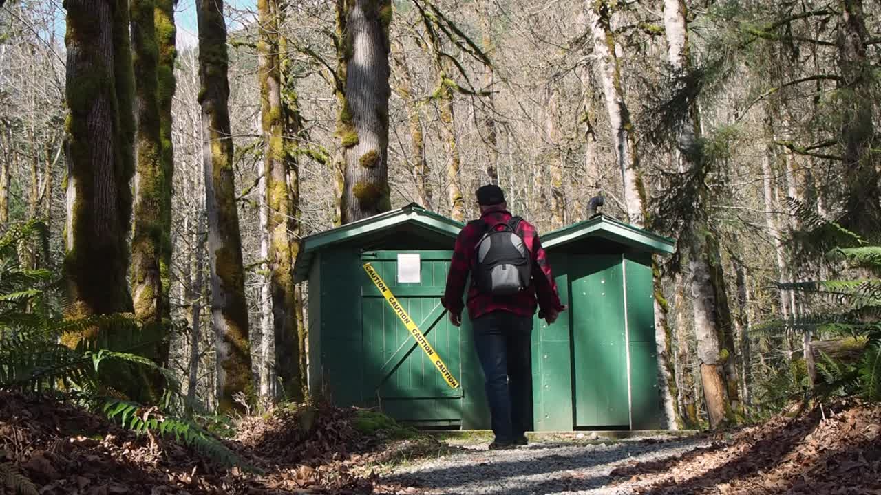 hombre en el bosque caminando hacia la letrina con cinta amarilla de precaución