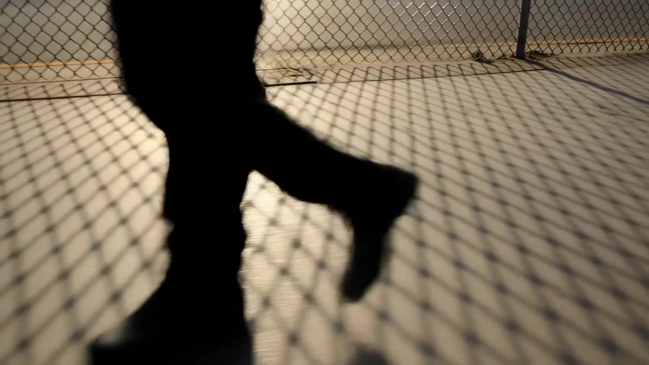 Silhouette of a person in motion walking behind a chainlink fence, captured during sunset in an urban outdoor setting