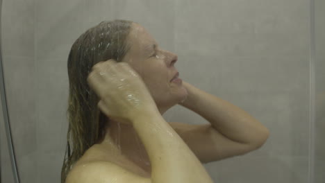 woman stepping under a running shower and cleansing her hair and face