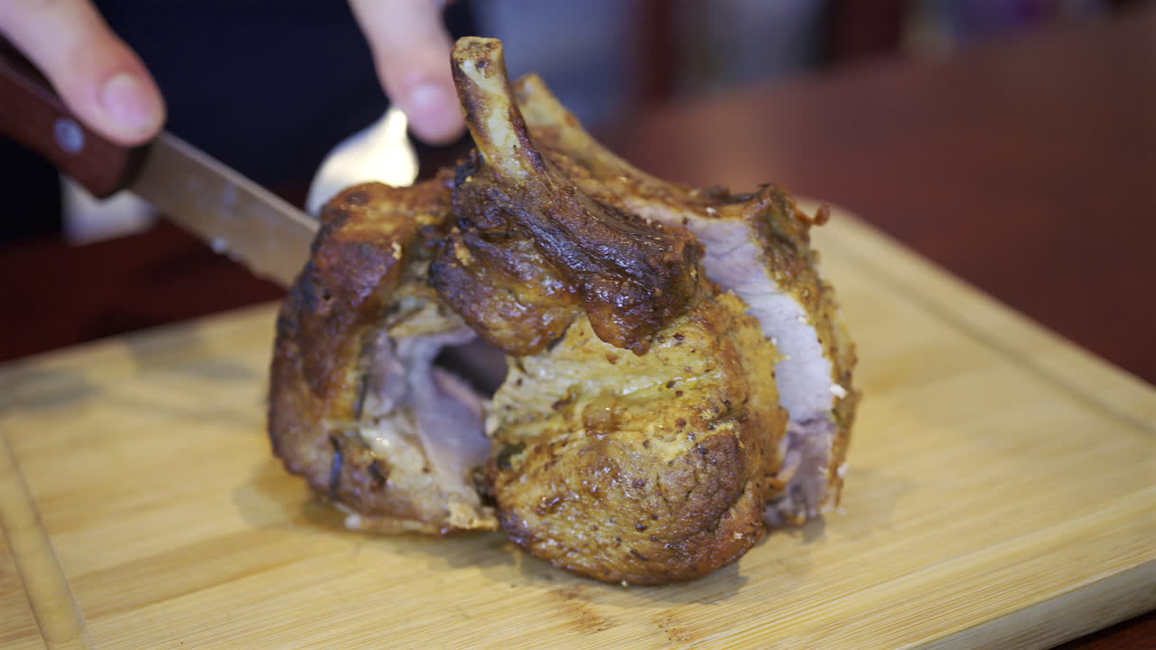 Close up of a man's hand cutting up a piece of pork on a wooden tray
