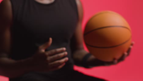 disparo de estudio de cerca de un jugador de baloncesto masculino lanzando la pelota de mano en mano contra un fondo rojo