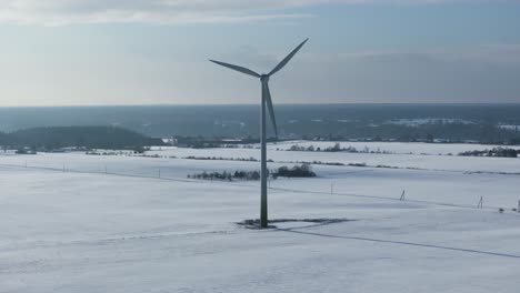 wind turbine slowly rotates in a snowy landscape in slow motion, with a backdrop of distant trees and fields