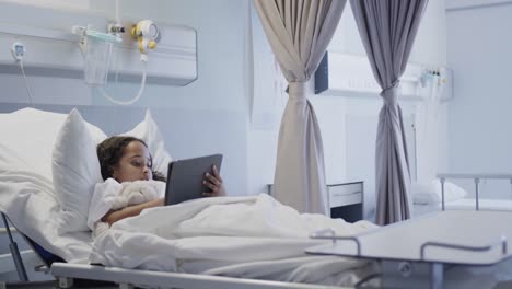 happy biracial sick girl patient using tablet in hospital bed in slow motion