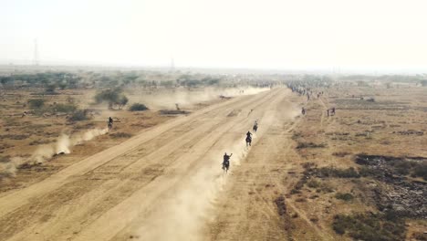 Vista-Aérea-De-Drones-De-Una-Carrera-De-Caballos-En-Un-Campo-Polvoriento-En-India