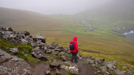 woman wearing wet red jacket hiking down villingardalsfjall, faroe islands