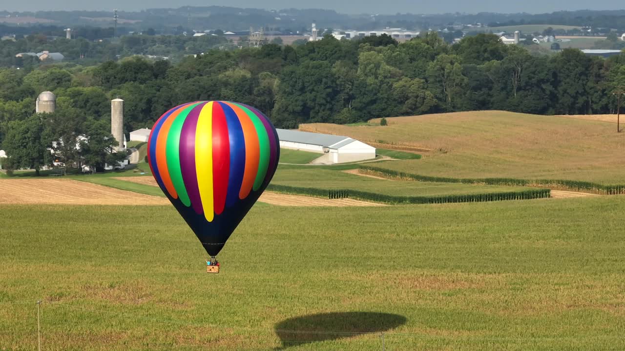 Droneoptagelse af en varmluftsballon, der svæver i luften over landbrugsmarker i udkanten af en by, Luftfoto