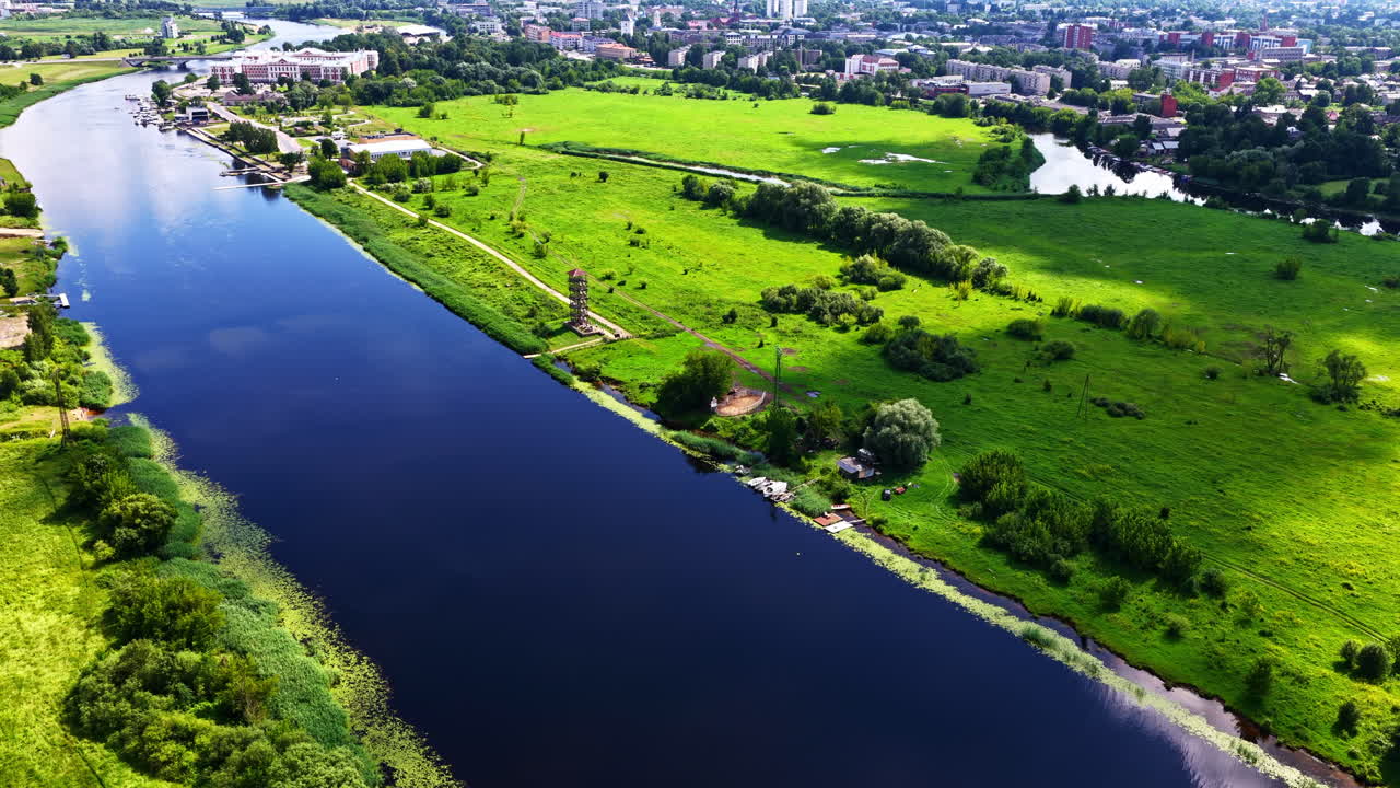 Canal flowing through farmland with trees lining water and midday sky reflections