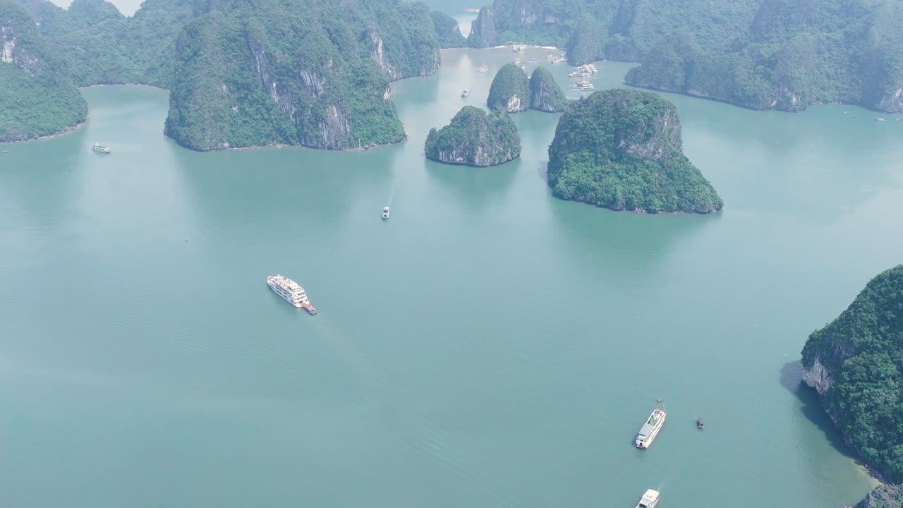Boats sail between limestone islands in calm turquoise water at Ha Long Bay, Vietnam
