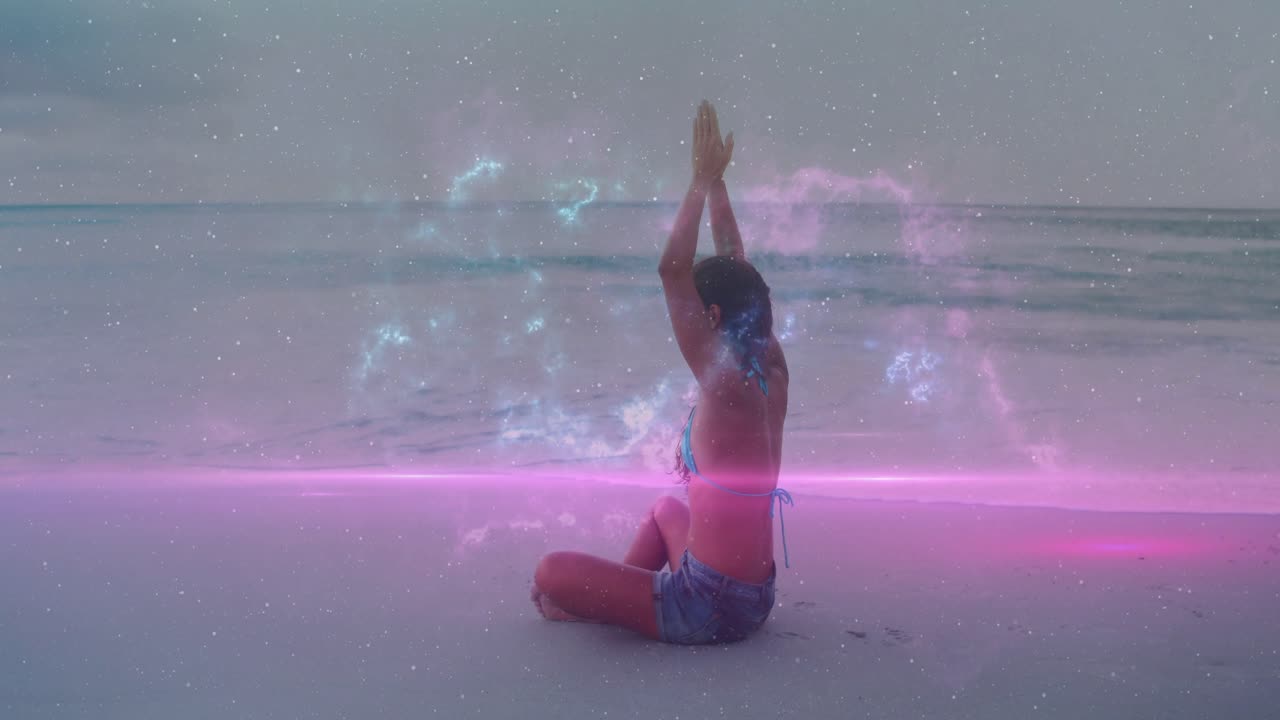 Donna seduta a gambe incrociate sulla spiaggia che alza le braccia, formando una fascia rosa e un bagliore di nebulosa per la salute