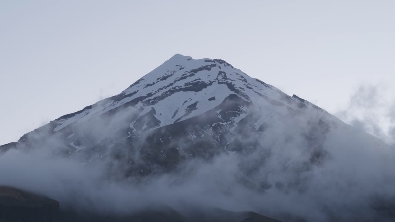 Clouds passing under the snowy peak of a mountain volcano at Mount Taranaki, New Zealand.