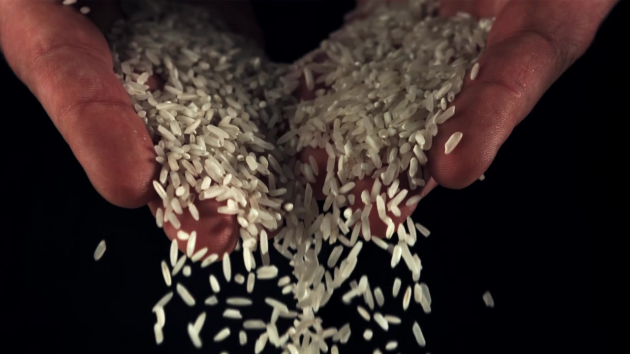 Hvide risgryn falder fra hænder i slowmotion