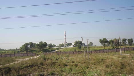 in a rural setting, there is a mosque with a tall tower, with a boundary wall enclosing the area.