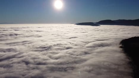 drone flight against the sun with a bright blue sky, camera slowly tilts towards the sea of ​​fog below, in switzerland